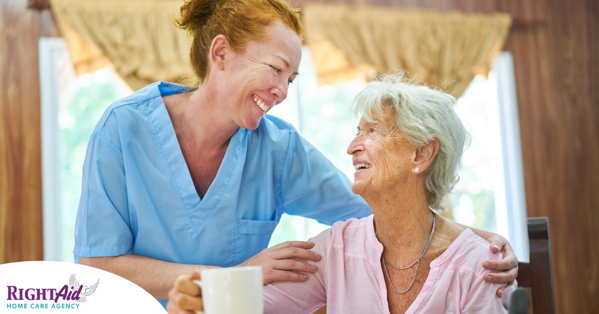 A caregiver and client smile while the caregiver hugs and helps the client, representing professional caregiving.