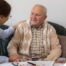 A caregiver compassionately listens to an older man, representing the kind of patience and empathy that help with communicating with clients who have dementia.