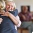 An older woman smiles as a younger woman visits her and hugs her, showing the effect that acts of kindness can have on senior loved ones.