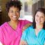 2 smiling women in scrubs represent RN supervisors and the good environment that can be promoted when they work together with caregivers for quality client care.