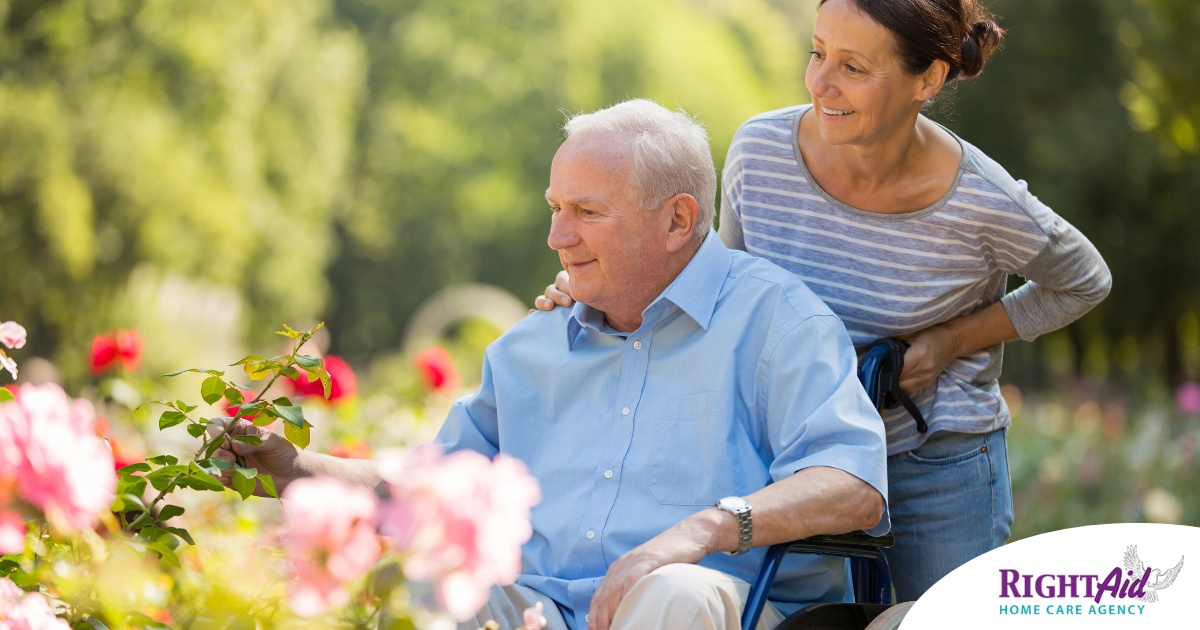 A caregiver brings an older adult with a wheelchair to see some flowers representing how professional caregivers can make outdoor activities accessible.